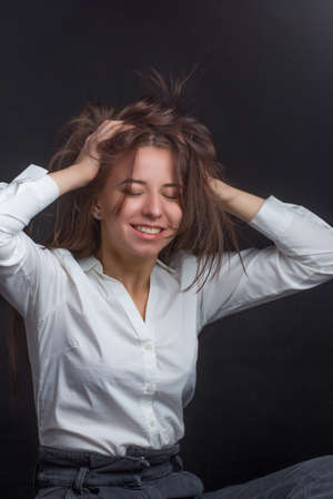 studio portrait of a young brown-haired woman, on a black background, she ruffled her hair with her handsの写真素材