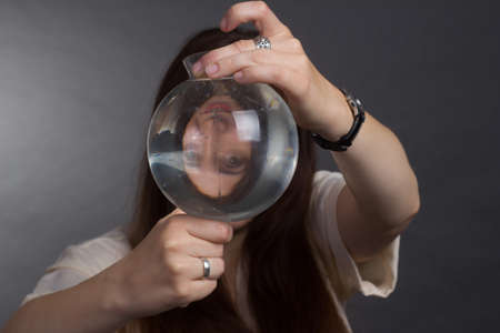 A brunette woman with long hair, wearing a beige blouse on a gray studio background. Looks at the...