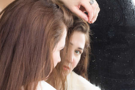 A brunette woman with long hair, wearing a beige blouse, Looks in the mirrorの写真素材