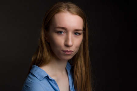A young woman in blue blouse, a portrait on a black studio background.