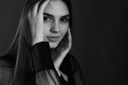 black and white portrait of a young woman with long brown hair. In black clothes on a black background.の写真素材