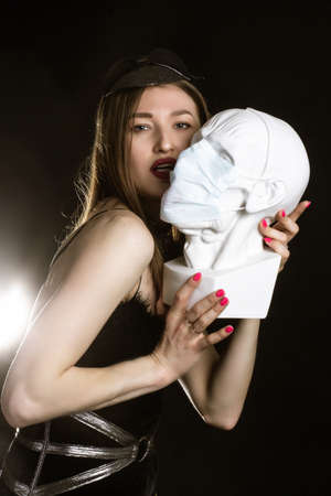 A young, beautiful woman clutches a plaster bust of a statue. Studio portrait.の写真素材