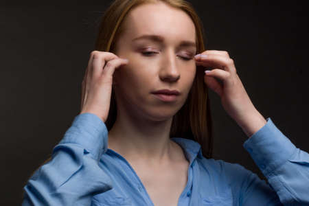 A young woman in a blue blouse, a portrait on a black studio background. he touches the skin of his face with his fingersの写真素材