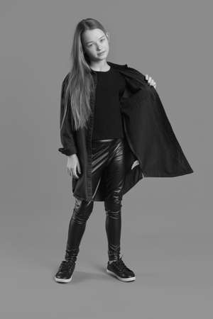 Black and whit Studio portrait of a young girl with brown hair, with long hair, on a gray background in black clothes and a leather jacketの写真素材