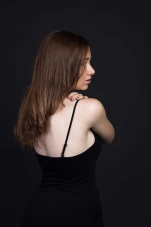 Young brown-haired woman, studio photo on a black background. She stands with her back to me, her arms crossed over her chest.の写真素材
