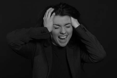 Black and white portrait of a young brunette woman in a studio on a black background, screaming, panickingの写真素材