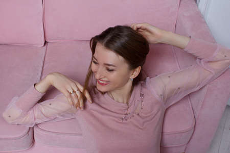 Studio portrait of a young woman with brown and long hair in pink clothes and underwear, on the background of a pink sofaの写真素材