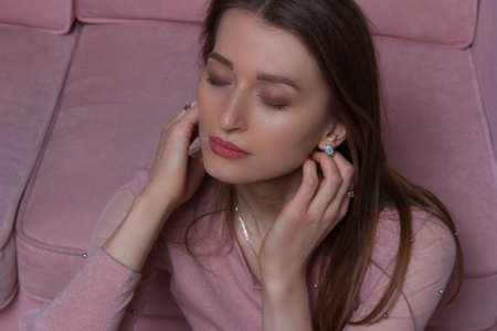Studio portrait of a young woman with brown and long hair in pink clothes and underwear, on the background of a pink sofaの写真素材