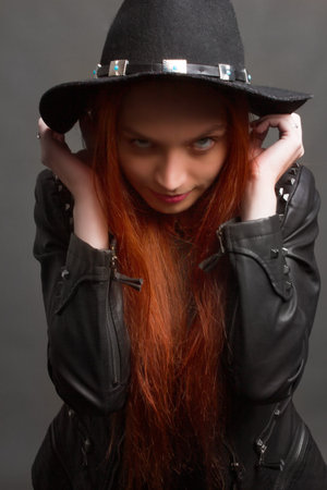 studio portrait of a young red-haired woman in black clothes on a black background. posing in a hatの写真素材
