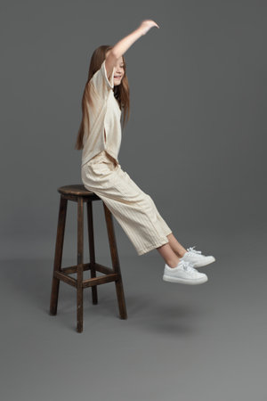 Studio portrait of a young girl with brown hair, with long hair, on a gray background in beige...