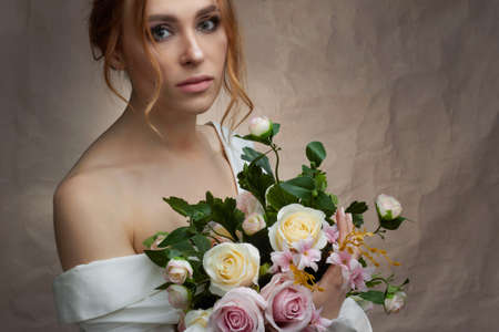 A girl in a white dress on a pink background with a bouquet of roses in her handsの写真素材