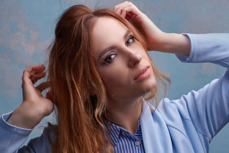 young beautiful Caucasian woman, in a blue suit, on a blue background. hands to hairの写真素材