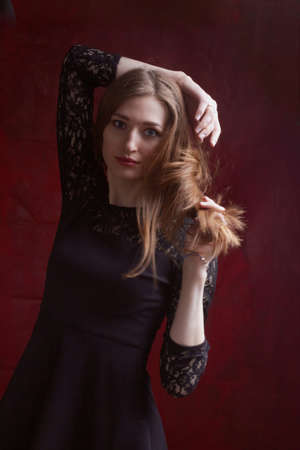 Portrait of a young woman with long brown hair, in a black dress on a red textured backgroundの写真素材