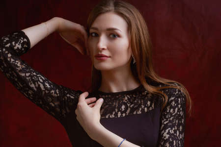 Portrait of a young woman with long brown hair, in a black dress on a red textured backgroundの写真素材