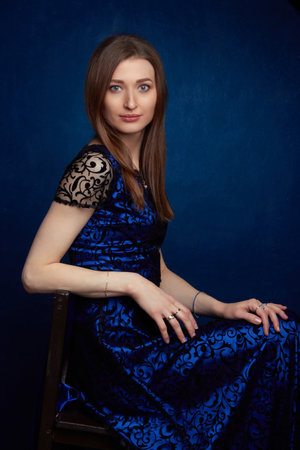 a woman with long brown hair, in a blue dress, studio portrait on a blue studio backgroundの写真素材