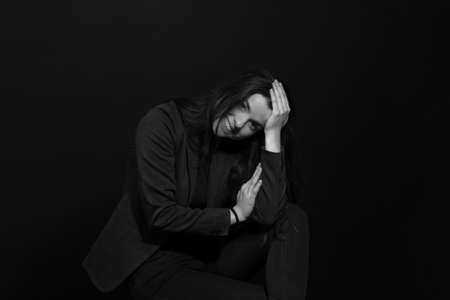 Black and white portrait of a young brunette woman in a studio on a black background, hand in hairの写真素材