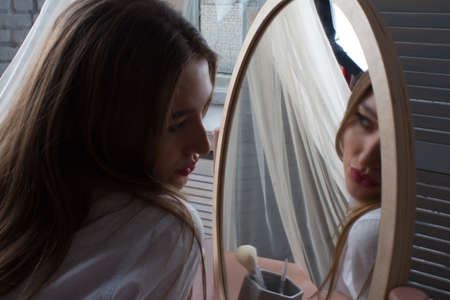 Amazing young woman doing her makeup in front of mirror. Portrait of beautiful girl near cosmetic tableの写真素材