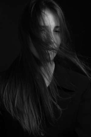 Black and white portrait of a young girl with long hair in a studio on a black backgroundの写真素材