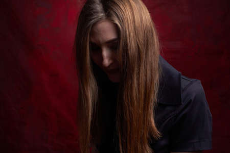 Portrait of a young woman with long brown hair, in a black dress on a red textured background