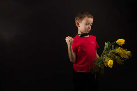 a boy with vitiligo in a red T-shirt with a bouquet of mimosaの写真素材