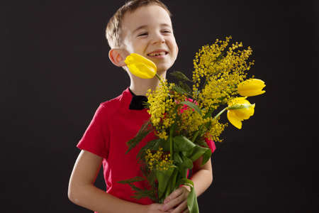 a boy with vitiligo in a red T-shirt with a bouquet of mimosa