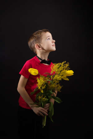 a boy with vitiligo in a red T-shirt with a bouquet of mimosaの写真素材