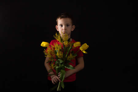 a boy with vitiligo in a red T-shirt with a bouquet of mimosa