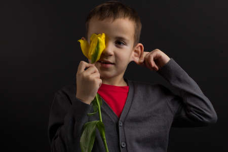 a boy with vitiligo in a red T-shirt, gray jacket, with a bouquet of yellow tulipsの写真素材
