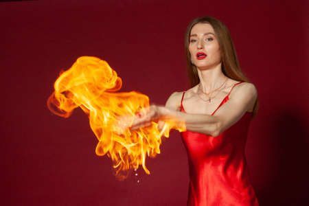 A young woman with long brown hair, in a red dress on a red background with fireの写真素材