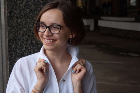 A young woman with short brown hair, wearing a white shirt, with glasses