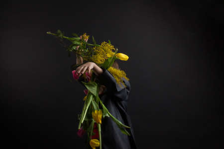a boy with vitiligo in a red T-shirt, gray jacket and bow tie, with a bouquet of mimosa and yellow...