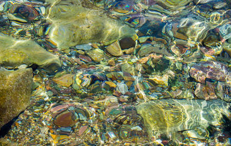 Seabed with pebbles under water with sunspots of light. View from aboveの写真素材