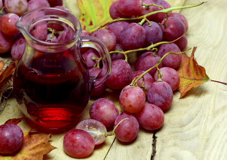 Red rose grapes bunch, glass jug bottle with red house wine or natural organic grape juice, and autumn leaves on wood background.の写真素材