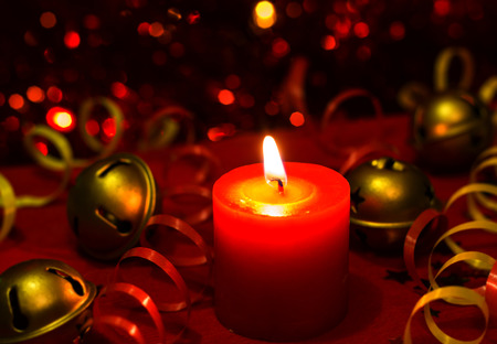 Christmas and New Year`s festive evening burning candle bokeh image. Greeting card lights Background concept with holiday tinsel, jingles bells, twisted ribbons and copyspace place for text.の写真素材