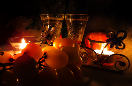 Christmas and New Year`s bokeh image. Two vintage champagne wineglass festive evening candle and gentle sweet green grapes. Greeting card Background holiday concept for restaurant or coffee party.の写真素材