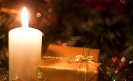 Christmas and New Year`s evening burning candle and present box wrapped in colorful wrapping paper with bows of gold ribbons. Retro style greeting card yellow toned background with holiday tinsel.の写真素材
