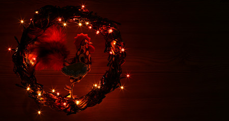 Happy New Year 2017 on the Chinese calendar of rooster template copyspace card with hand made rooster in decorated Christmas wreath. Garlands of colored light bulbs in night. Black wooden background.の写真素材