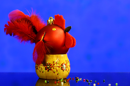 Christmas background with red balls hand made decorated as rooster on wooden stand. Blue holiday...