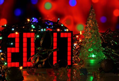 Happy New Year 2017 colorful greeting card real photo with green glass Christmas tree on bokeh background. Party poster, banner or invitation. Mirror surface. Number formed from red digital clock.の写真素材