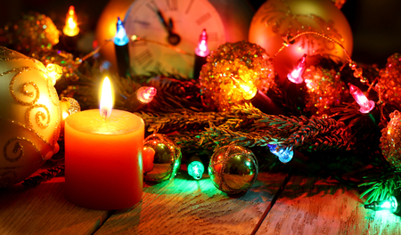 New Year`s card with Christmas tree fir branches, midnight clock, burning candle, golden pine cones, balls, garland lights on vertical old wooden desk table background. Big copyspace for holiday congratulations.の写真素材