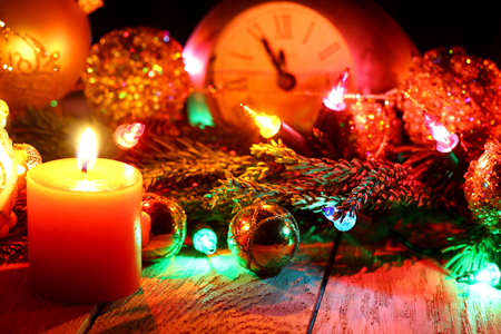 New Year`s card with Christmas tree fir branches, midnight clock, burning candle, golden pine cones, balls, garland lights on vertical old wooden desk table background. Big copyspace for holiday congratulations.の写真素材