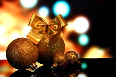 Christmas gold ball decorations with Bow of golden ribbons on a black mirror reflection surface and lights bokeh backgroundの写真素材