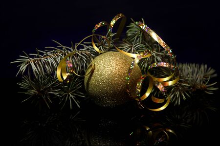 Christmas gold decorations ball with fir tree brunch, golden ribbons on a black mirror reflection surface and dark blue bokeh background. New year`s vintage country style card.の写真素材