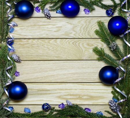 New Year`s border frame from Christmas tree fir branches, silver pine cones, ribbons, blue balls on vertical old wooden desk table background. Big copyspace for holiday congratulations.の写真素材