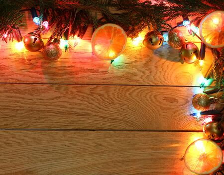 New Year`s top border, frame from Christmas tree fir branches, golden decorations balls, garland colorful lights on vertical wooden desk table background. Big copyspace for holiday congratulations.の写真素材