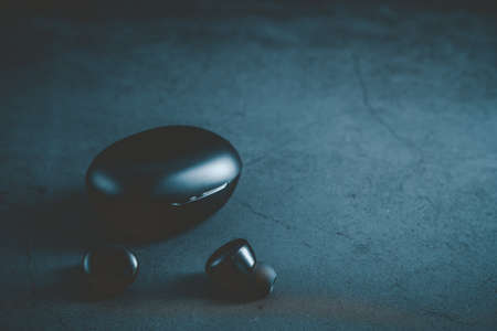 Black wireless earphones and their holster are isolated on a black background. True wireless stereo earphones. Wireless earphones with casing closed.の写真素材