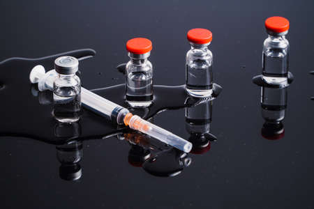 Medical vials and syringes on a black background with reflection