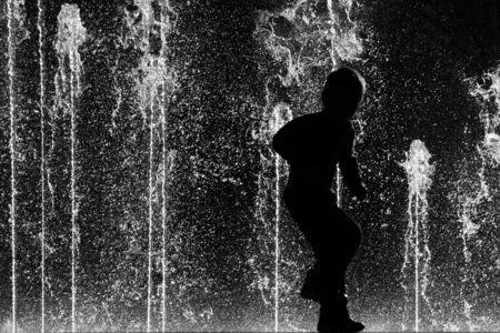 Silhouette of a young child joyfully dancing with fountains in the backgroundの写真素材
