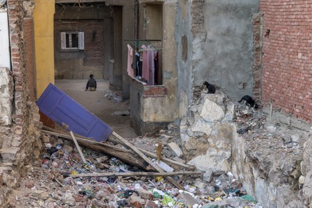 Poverty is noted near crumbled building in Cairo, Egypt with poor boy sitting on a ballの写真素材