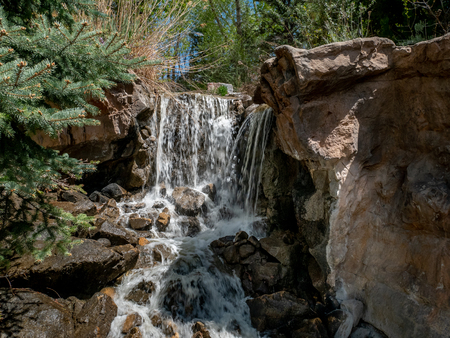 Small waterfall flowing through a park with flowers and trees all aroundの写真素材